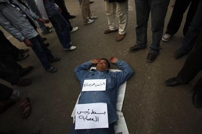 Дэманстрант спіць на плошчы Тахрыр. На ім надпісы: «Далоў галоўнага бандыта» і «Народу рашаць!»